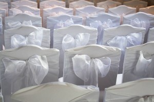 detail of chair back decorated for a wedding. white bows on white covers