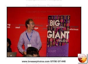 Luke Quilter, Big Giant adressing an audience with his company pull up banner beside him