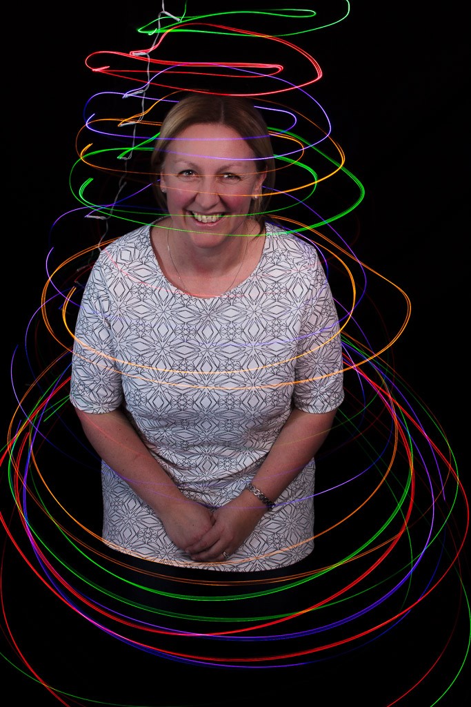 portrait of a woman against a dark background with light trails around her in multiple colours