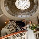 Bride and groom walk down spiral stairs and above the is an oculus.