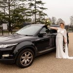 Bride poses with her sweet ride (a black range rover car)