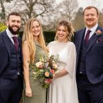 Bride, groom, Best Man and bridesmaid pose for a formal photo in a garden