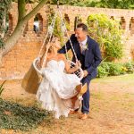 Wedding couple laugh as she sits in a rope swing from a tree