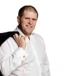 Man with his jacket casually held over his shoulder posing for the camera against a white background