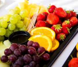 A platter of mixed fruit - strawberries, slices of orange, green and black grapes
