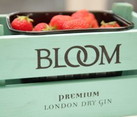 Close up of a green wooden box marked 'Bloom Gin' with a punnet of strawberries