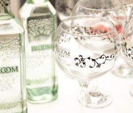 Two clear Bloom Gin bottles with large gin goblets besides the bottles
