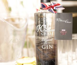 A bottle of William Chase gin with a crisp apple beside it. There is a stylish label attached to the bottle