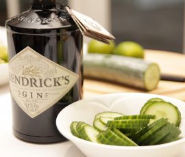 Bottle of Hendrick's gin with a bowl of sliced cucumber in the foreground. Behind it and out of focus is a cut cucumber