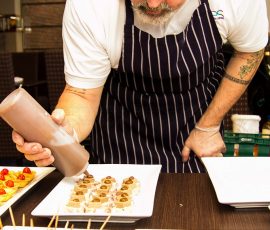 Chef finishing a plate of hors d'oeuvres with dressing. Other plates in the foreground are ready for service