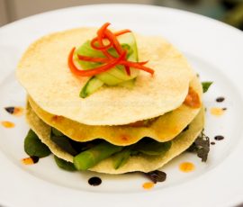 Close up of a stack of three papadums layered with vegetables and sauce on a white plate