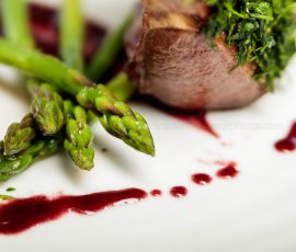 Close up of asparagus tips which accompany a rack of lamb. A red wine jus is dabbled across the white plate
