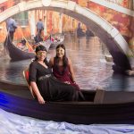 Two women on a fake gondola against a backdrop that appears to be a Venitian canal