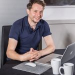 Male sitting at table with laptop computer, mouse pad and coffee cups